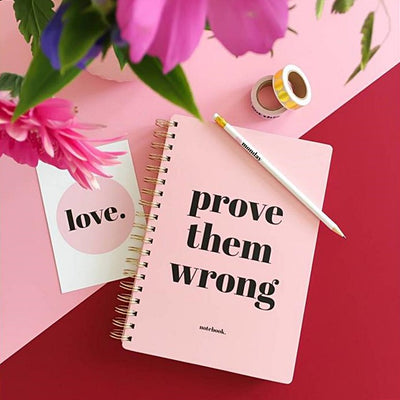 Libreta rosa con espiral dorada y frase "prove them wrong", ideal para notas creativas y organización.